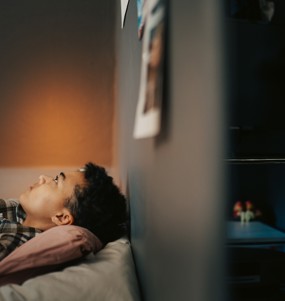 Kille ligger på säng och tittar upp i taket.