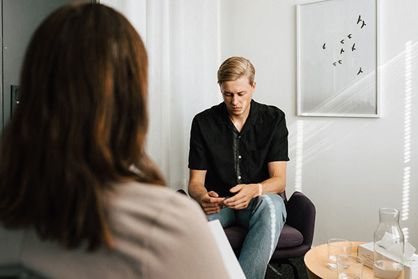 En man sitter i en stol och tittar ner i sitt knä medan han pratar med en kvinna.