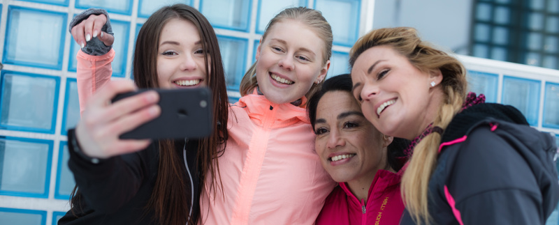 Två kvinnor och två flickor i fritidskläder tar en selfie och ler mot kameran