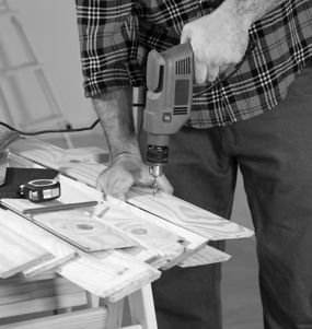 En man som Står Med En Elektrisk Handborr Och Borrar I Trä