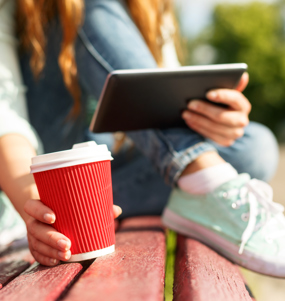 Ung kvinna sitter på en parkbänk med en kaffemugg. 
