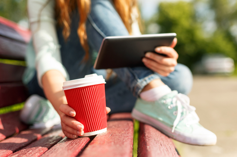 En ung kvinna sitter på en parkbänk med en kaffemugg.