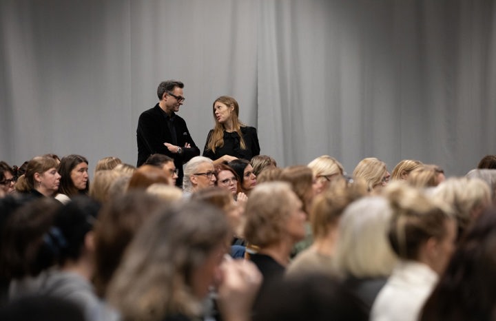 En man och en kvinna som samtalar ståendes. Framför dem sitter ett stort antal människor.